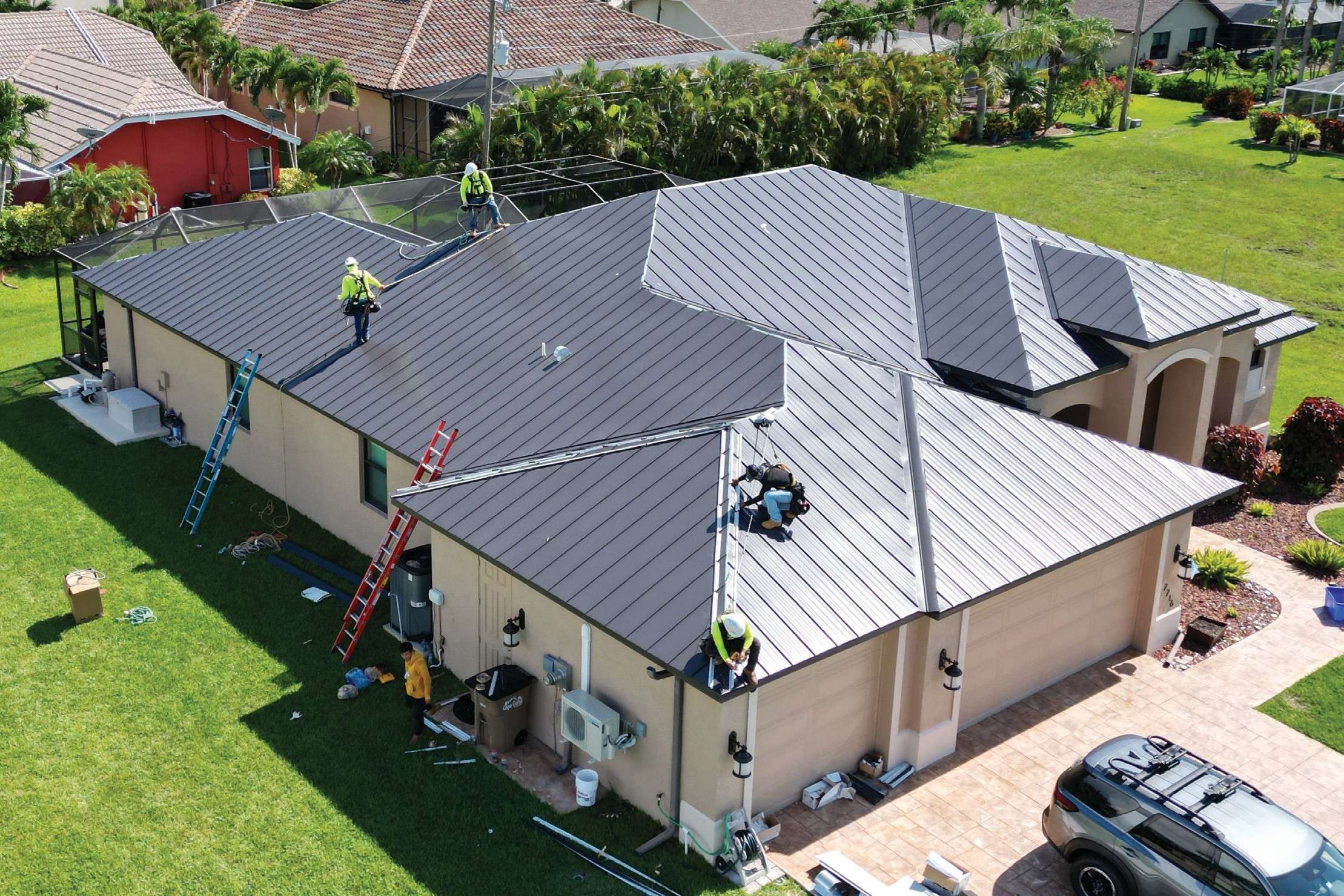 Roofers installing a dark standing-seam metal roof on a single-story house